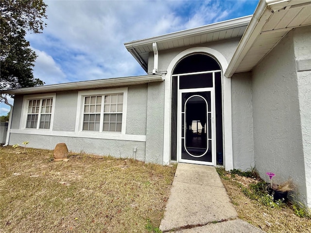 doorway to property with a lawn and stucco siding