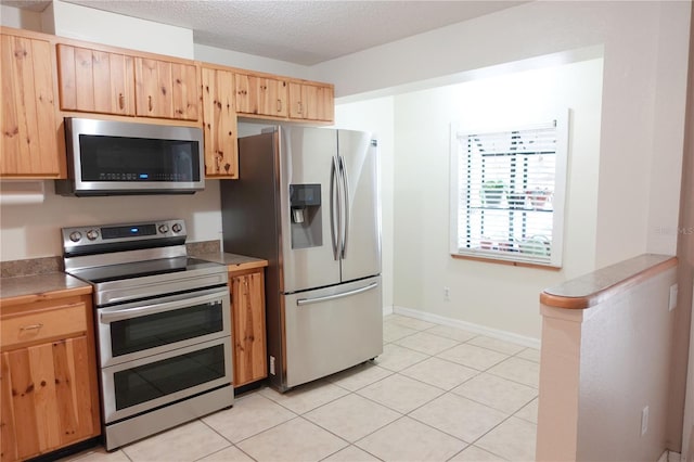 kitchen with stainless steel appliances, a textured ceiling, and light tile patterned floors