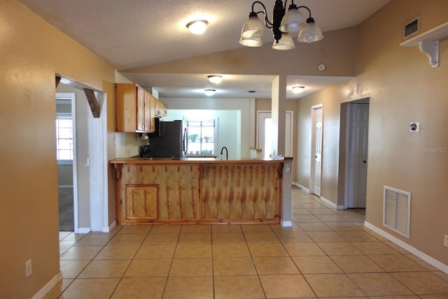 kitchen featuring stainless steel fridge, plenty of natural light, light tile patterned flooring, vaulted ceiling, and kitchen peninsula