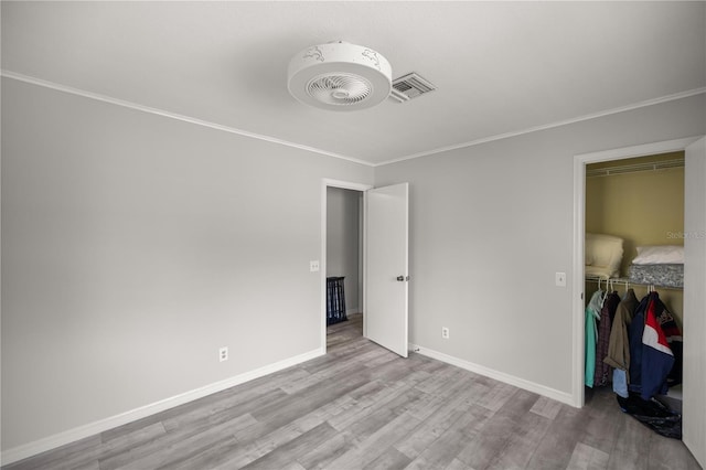 unfurnished bedroom featuring a walk in closet, light hardwood / wood-style flooring, ornamental molding, and a closet