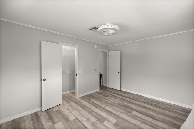 unfurnished bedroom featuring crown molding, a walk in closet, light wood-type flooring, and a closet