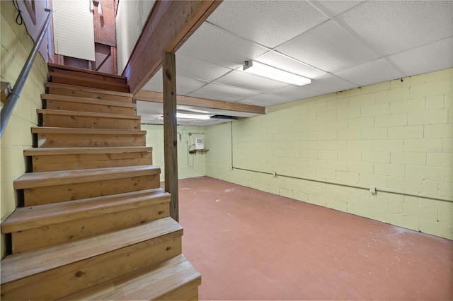 staircase with concrete flooring, concrete block wall, and a paneled ceiling