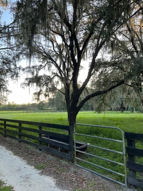 view of gate with a rural view, fence, and a lawn