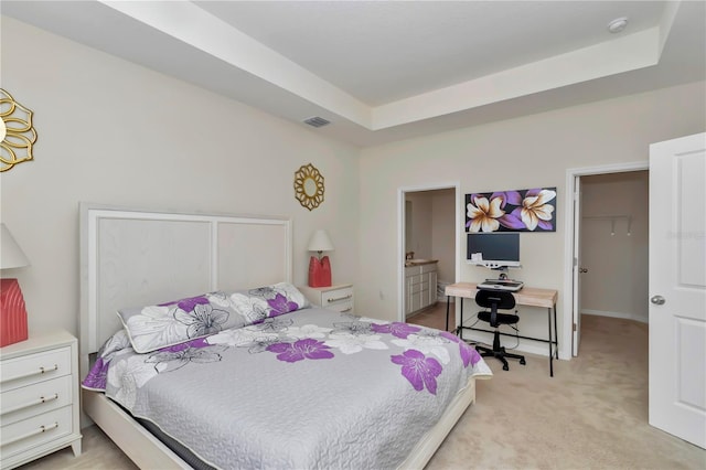 bedroom featuring connected bathroom, a raised ceiling, and light carpet