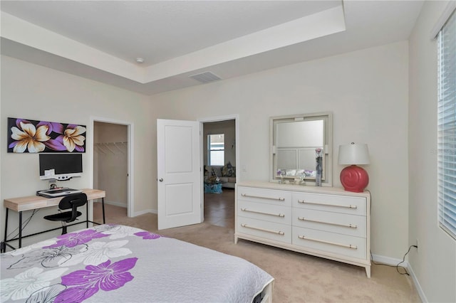 bedroom with light carpet, a tray ceiling, a walk in closet, and a closet