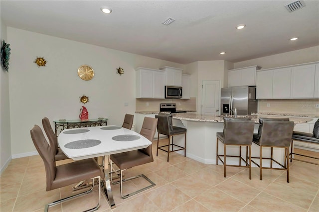 kitchen featuring a breakfast bar area, a center island with sink, appliances with stainless steel finishes, light stone countertops, and white cabinets