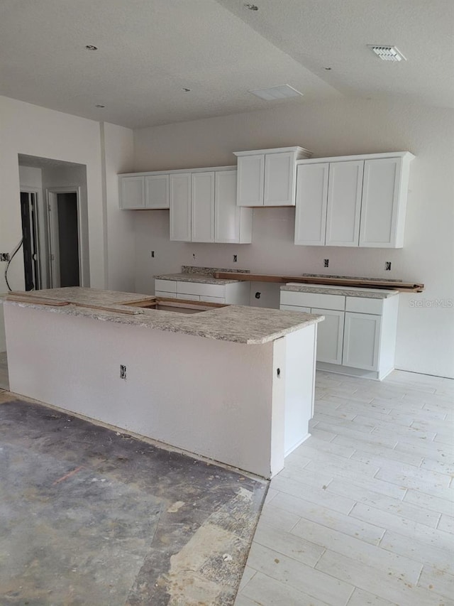 kitchen featuring vaulted ceiling, visible vents, and white cabinets