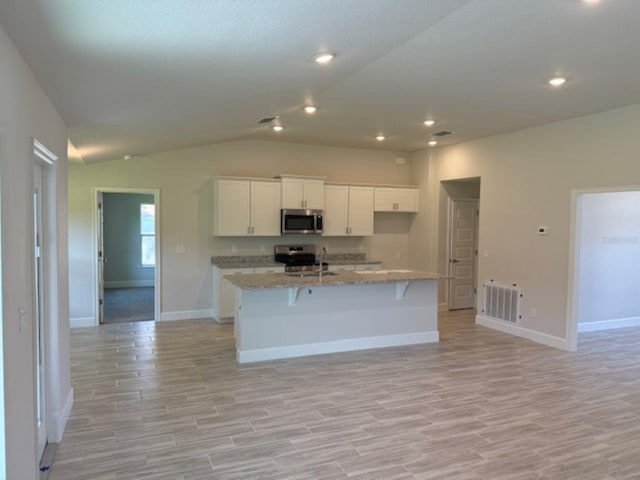 13 NW 45th Loop, Ocala, FL 34475 - kitchen with stainless steel appliances, light wood-type flooring, white cabinetry, lofted ceiling, and a center island with sink