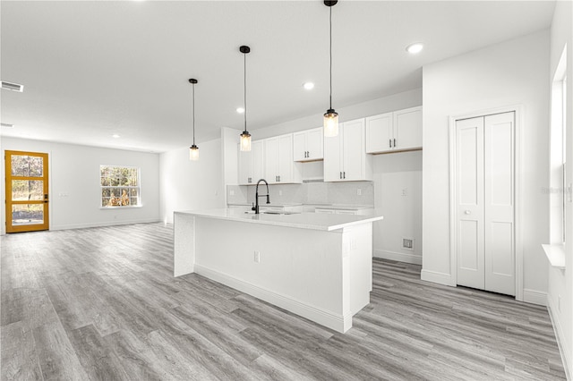 kitchen featuring white cabinetry, hanging light fixtures, light wood-type flooring, a kitchen island with sink, and backsplash