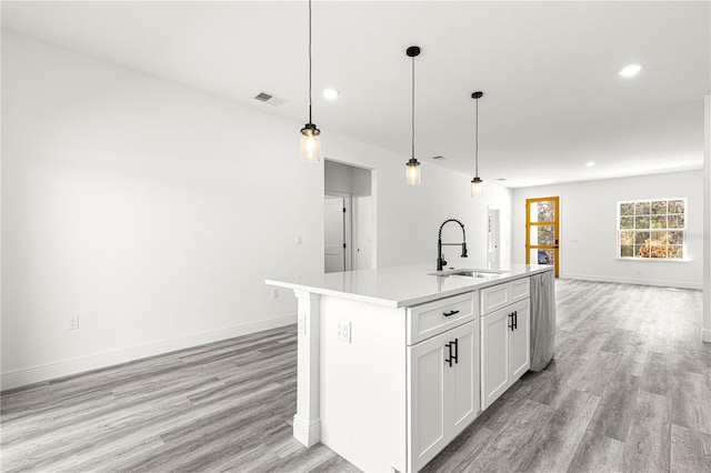 kitchen featuring sink, hanging light fixtures, a center island with sink, light hardwood / wood-style floors, and white cabinets