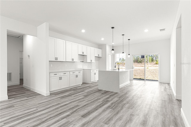 kitchen featuring white cabinetry, hanging light fixtures, sink, and an island with sink