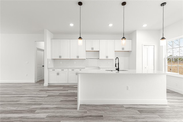 kitchen with a kitchen island with sink, white cabinetry, pendant lighting, and decorative backsplash