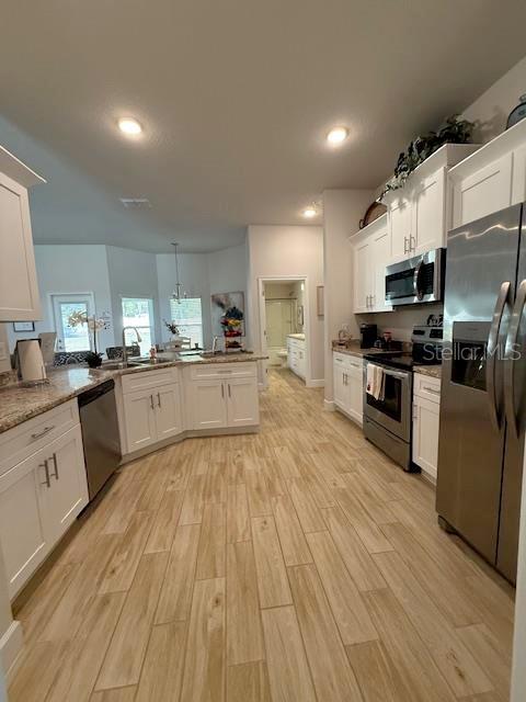 kitchen with light wood-style flooring, a peninsula, a sink, white cabinetry, and appliances with stainless steel finishes