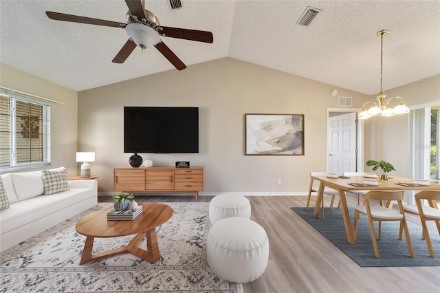 living room featuring vaulted ceiling, ceiling fan with notable chandelier, a textured ceiling, and light hardwood / wood-style floors