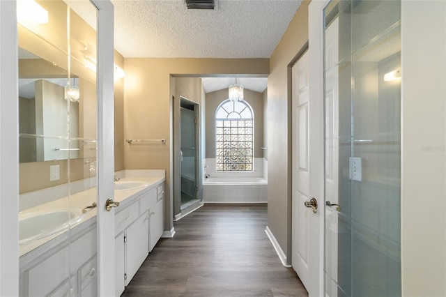 bathroom with hardwood / wood-style flooring, vanity, tiled bath, and a textured ceiling