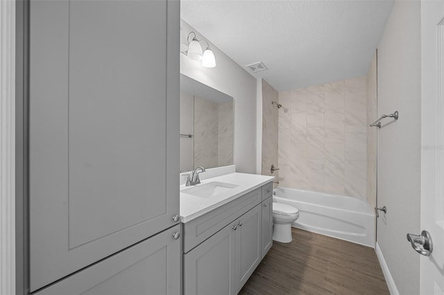 full bathroom with toilet, wood-type flooring, a textured ceiling, vanity, and tiled shower / bath combo