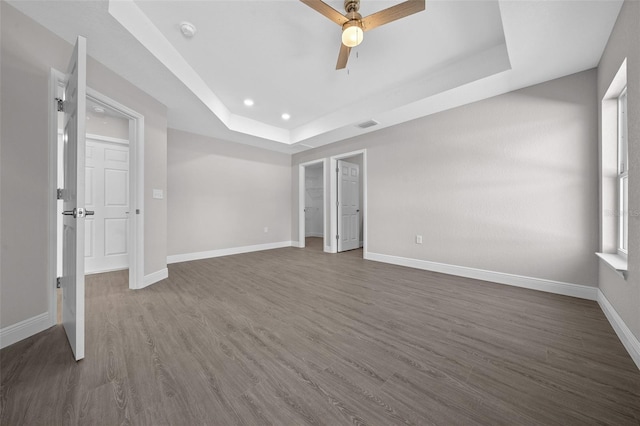 unfurnished bedroom with ceiling fan, a tray ceiling, and dark hardwood / wood-style flooring