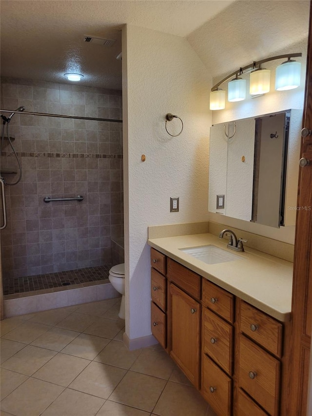 bathroom with tile patterned flooring, vanity, a tile shower, a textured ceiling, and toilet