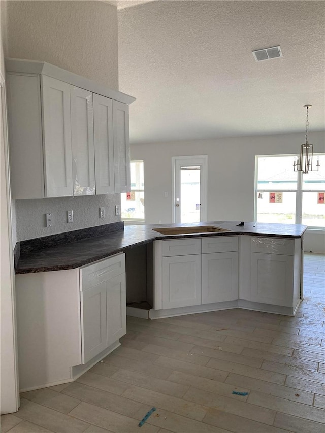 kitchen with pendant lighting, an inviting chandelier, a textured ceiling, white cabinets, and light wood-type flooring