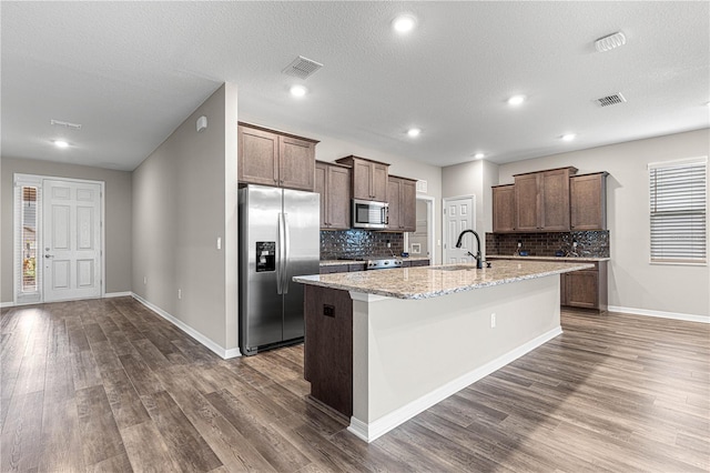 kitchen with a kitchen island with sink, light stone counters, dark hardwood / wood-style floors, and appliances with stainless steel finishes