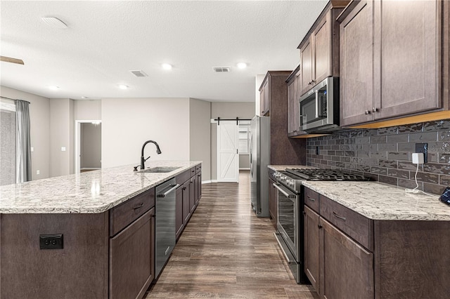 kitchen with sink, a center island with sink, a barn door, and appliances with stainless steel finishes