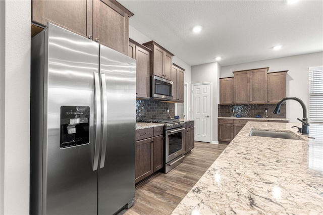 kitchen featuring sink, dark brown cabinets, appliances with stainless steel finishes, dark hardwood / wood-style flooring, and light stone countertops