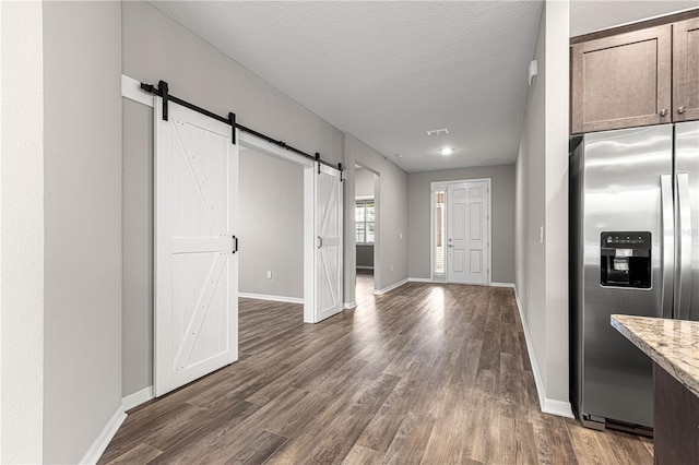 interior space with stainless steel refrigerator with ice dispenser, a textured ceiling, dark hardwood / wood-style flooring, a barn door, and light stone countertops