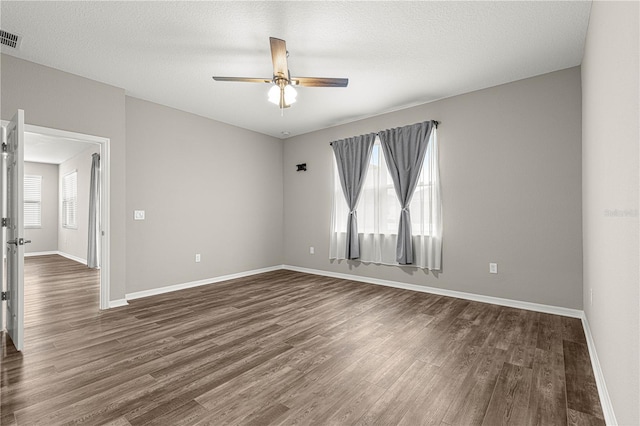 empty room with ceiling fan, a healthy amount of sunlight, dark hardwood / wood-style floors, and a textured ceiling