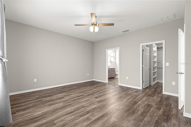 unfurnished bedroom featuring ensuite bathroom, a walk in closet, dark hardwood / wood-style flooring, and a closet