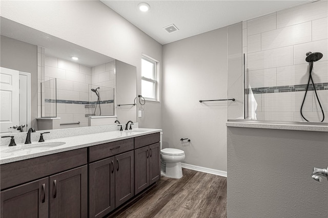 bathroom with hardwood / wood-style flooring, vanity, tiled shower, and toilet