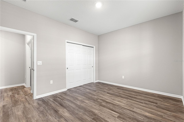 unfurnished bedroom with a textured ceiling, dark hardwood / wood-style flooring, and a closet