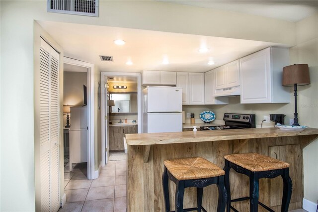 kitchen featuring a kitchen bar, stainless steel electric range oven, kitchen peninsula, white fridge, and white cabinets