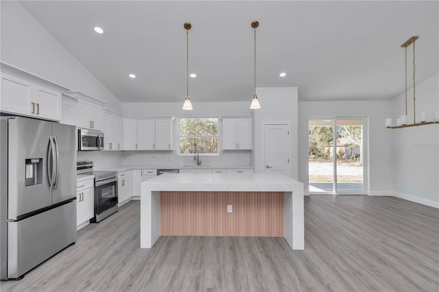 kitchen with appliances with stainless steel finishes, white cabinetry, hanging light fixtures, a center island, and light stone counters