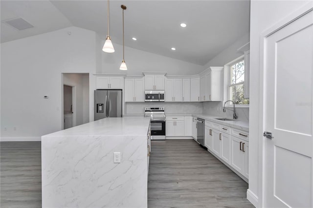 kitchen featuring sink, white cabinetry, light stone counters, decorative light fixtures, and appliances with stainless steel finishes