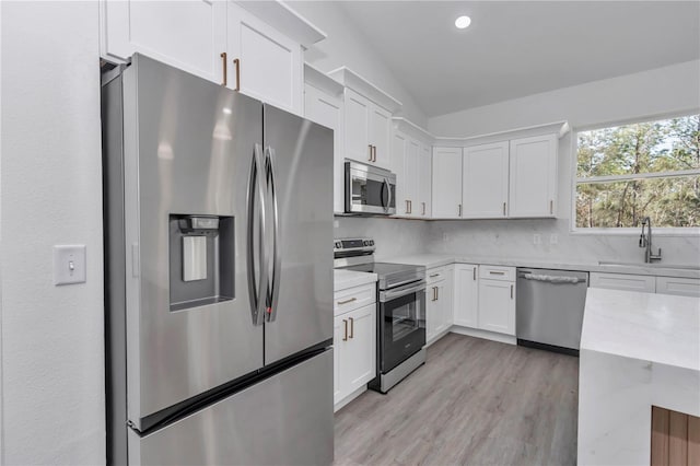 kitchen featuring appliances with stainless steel finishes, white cabinetry, sink, decorative backsplash, and light wood-type flooring