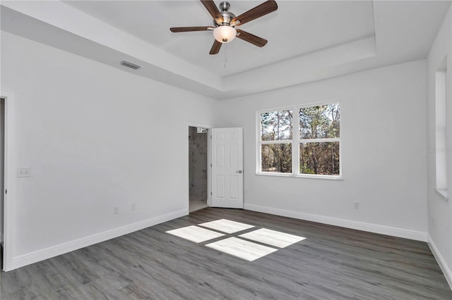 empty room with ceiling fan, dark hardwood / wood-style flooring, and a raised ceiling