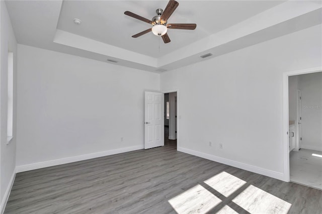 spare room featuring dark wood-type flooring, a raised ceiling, and ceiling fan