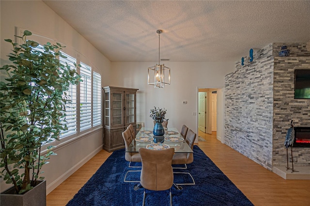 dining room featuring a notable chandelier, a textured ceiling, a fireplace, and light hardwood / wood-style floors