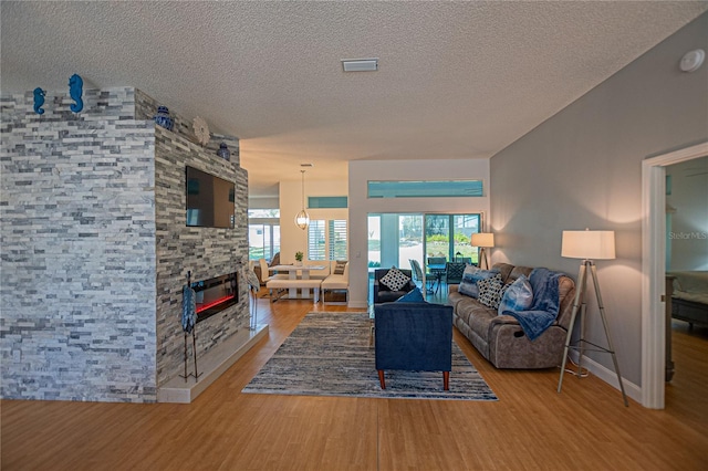 living room featuring wood-type flooring, a stone fireplace, and a textured ceiling