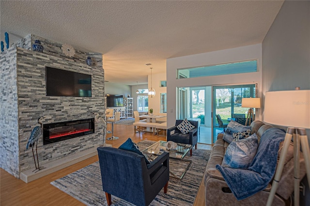 living room featuring an inviting chandelier, a stone fireplace, wood-type flooring, and a textured ceiling