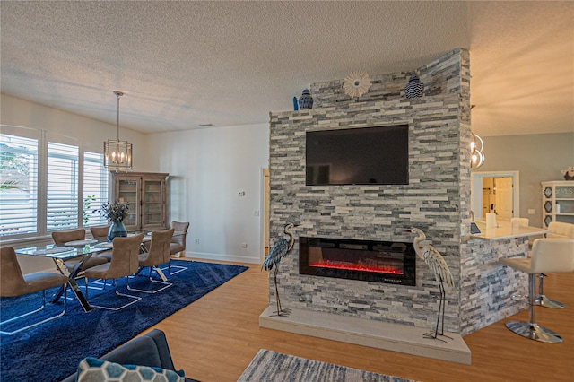 living room featuring wood-type flooring, a fireplace, a chandelier, and a textured ceiling