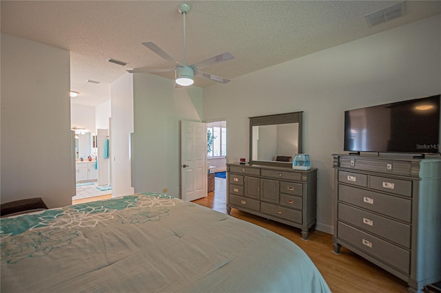 bedroom with ceiling fan, ensuite bath, light hardwood / wood-style flooring, and a textured ceiling