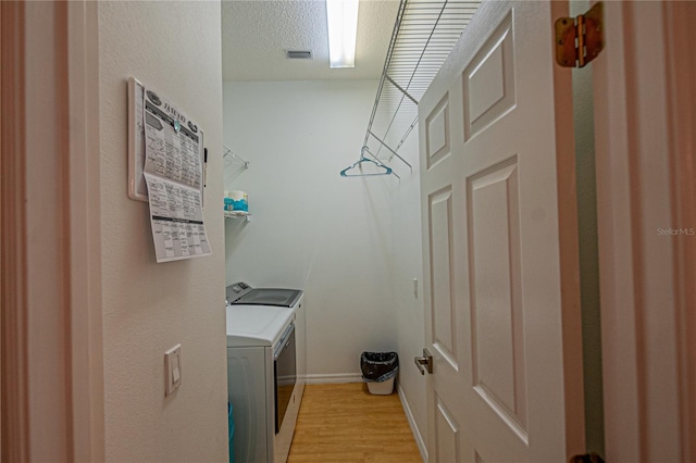 laundry room featuring a textured ceiling, washer and clothes dryer, and light hardwood / wood-style floors