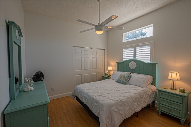 bedroom featuring ceiling fan, a towering ceiling, a textured ceiling, dark hardwood / wood-style flooring, and a closet