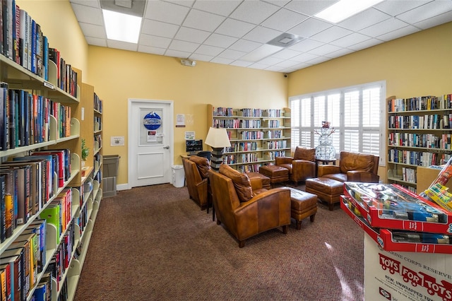 living area featuring a paneled ceiling and dark colored carpet