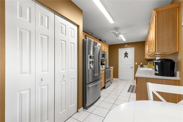 kitchen featuring sink, light tile patterned floors, ceiling fan, stainless steel appliances, and a textured ceiling