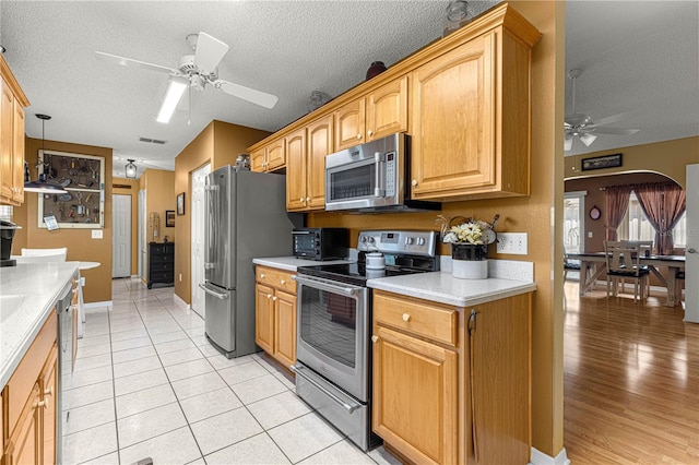 kitchen with light tile patterned floors, ceiling fan, hanging light fixtures, stainless steel appliances, and a textured ceiling