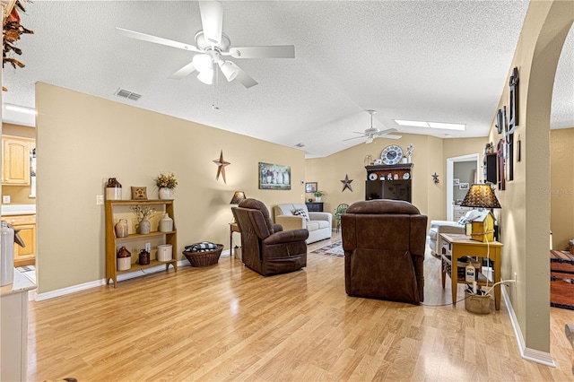 living room featuring lofted ceiling with skylight, a textured ceiling, ceiling fan, and light hardwood / wood-style flooring