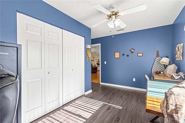 bedroom with ceiling fan, dark hardwood / wood-style floors, a textured ceiling, and a closet