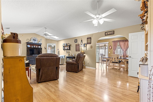 living room featuring vaulted ceiling, light wood-type flooring, a textured ceiling, and ceiling fan